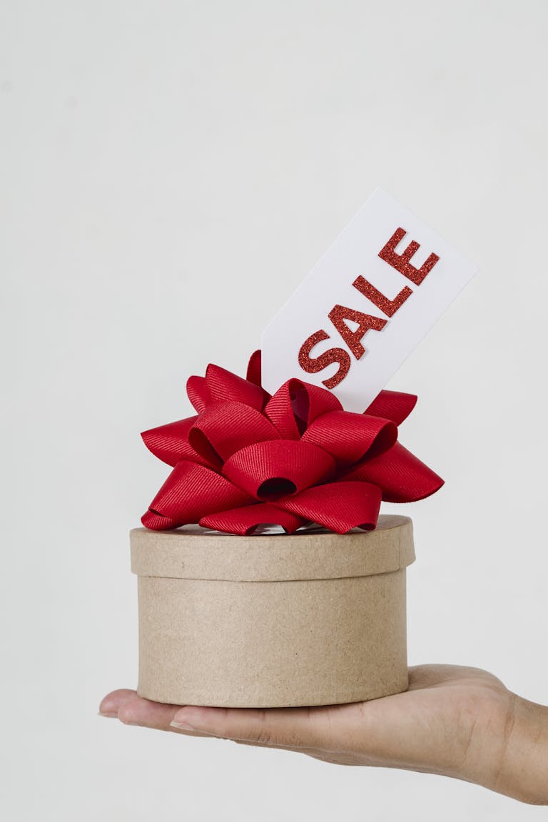 Close-up of a gift box with a red ribbon and sale tag on a hand.