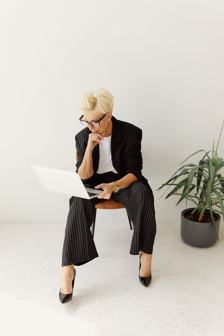 Professional woman in business attire working on laptop indoors, displaying focus and style.